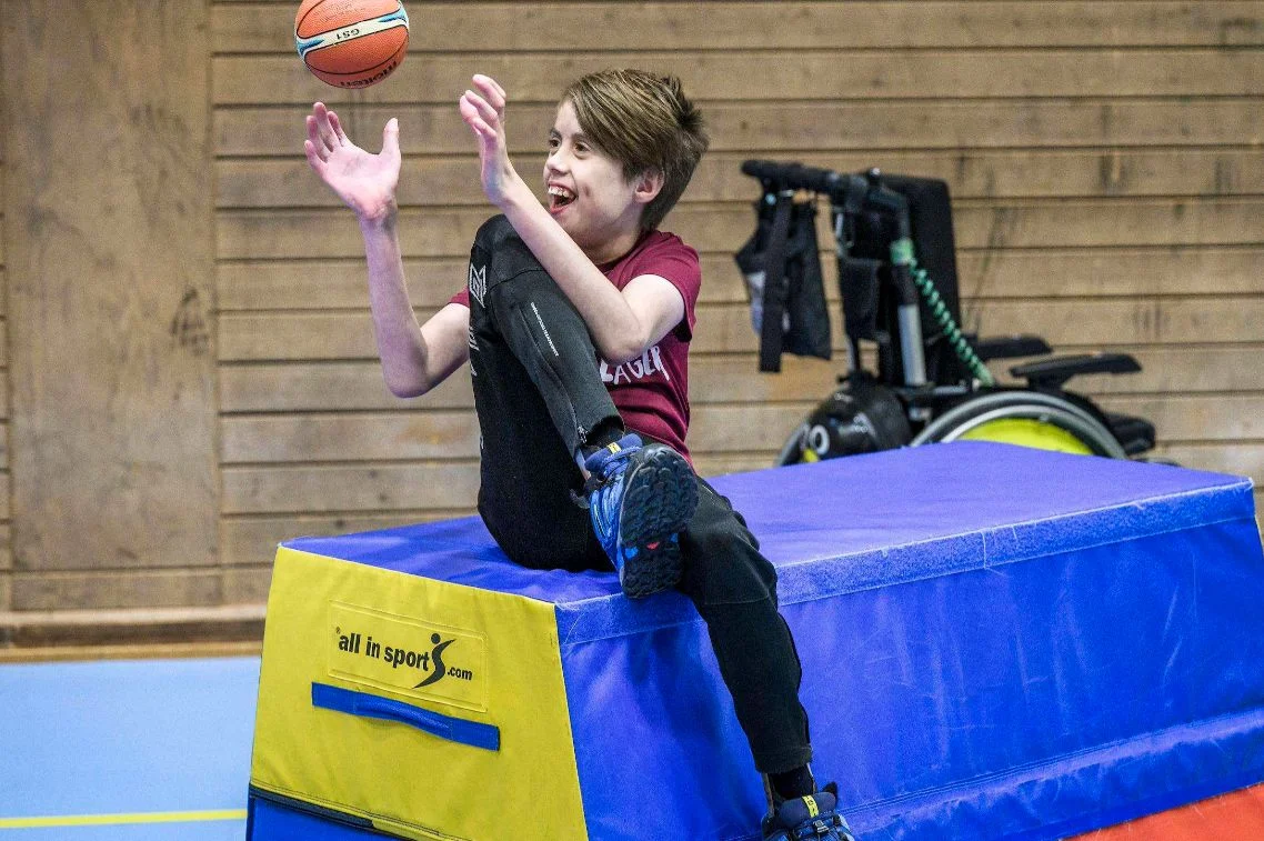 En deltagare kastar en basketboll sittande på en mjuk plint.