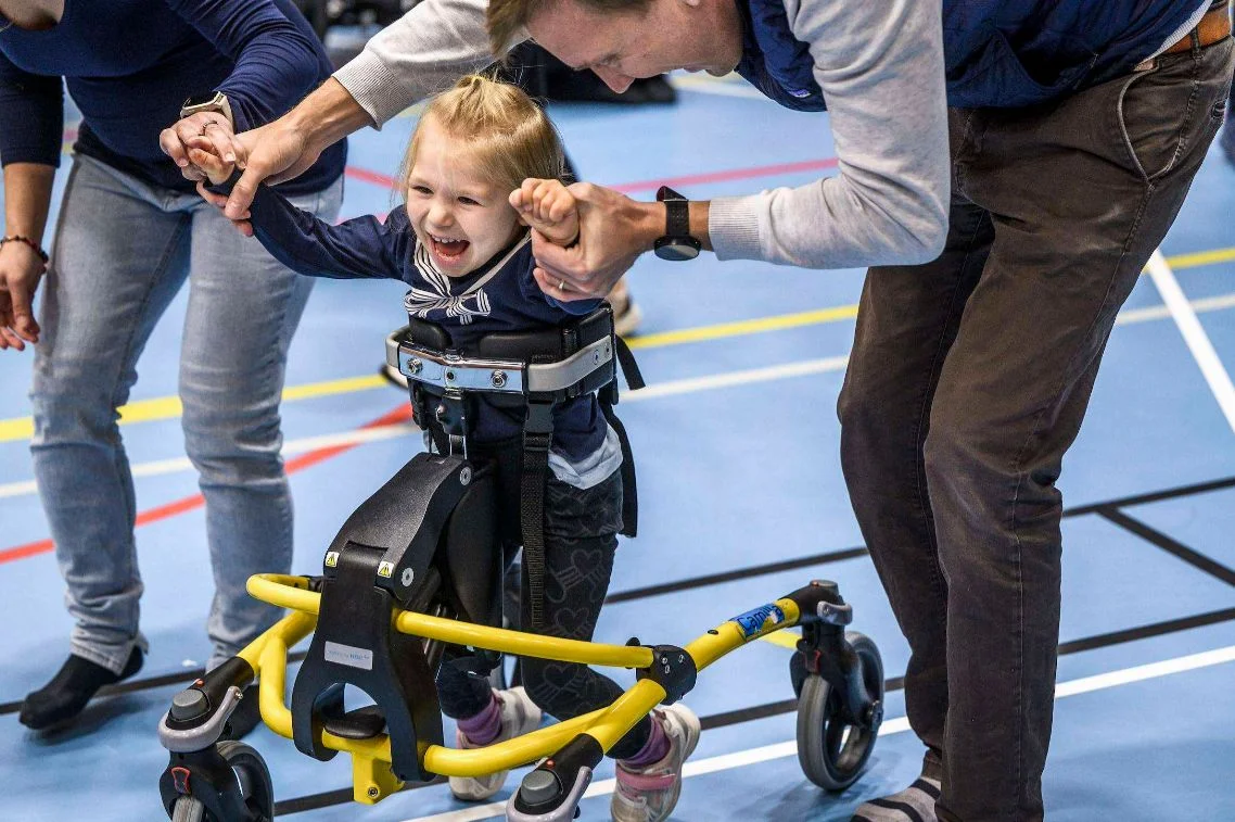Ett barn tränar med gånghjälpmedel och stöd av vuxna.